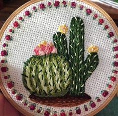 a hand embroidered cactus with pink flowers on it's back and green stems in the center