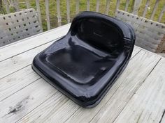 an empty black plastic chair sitting on top of a wooden table next to a fence