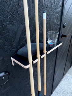 two baseball bats and a glass on a shelf outside the door to a building with black walls