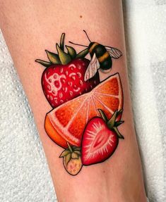 a strawberry, orange and bee tattoo on the leg