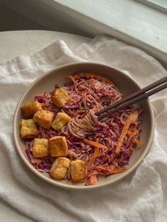 a bowl filled with noodles and vegetables on top of a white napkin next to a window