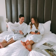 a man and woman in white robes sitting on a bed with their feet propped up