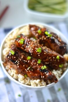 a bowl filled with rice and meat covered in sesame seed sauce, garnished with green onions