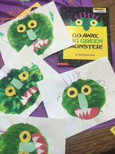 four children's handprints with green monster faces on them, sitting on a table