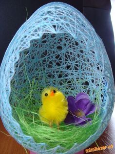 a small yellow bird sitting in a blue wire nest with purple crocsants