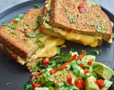 two grilled sandwiches with cheese, lettuce and tomatoes on a black plate