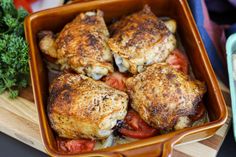 chicken and tomatoes in a casserole dish on a cutting board