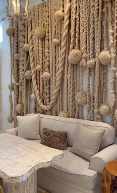 a white couch sitting next to a wooden table in front of a wall covered with rope