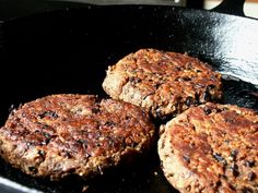 three hamburger patties cooking in a frying pan