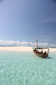 a boat that is floating in the water near some sand and blue sky with people on it