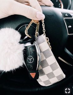 a hand holding a car key chain with a fur ball hanging from it's center console