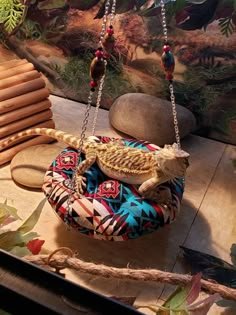 a small lizard sitting on top of a colorful cushion hanging from a chain over a wooden table