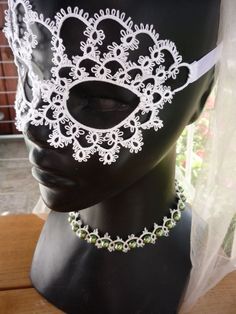 a mannequin head with a white mask on it's face and green beads around the neck