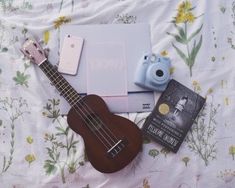 a ukulele, camera, book and other items are laying on a bed