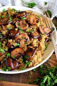 a white bowl filled with rice and mushrooms on top of a wooden table next to a fork