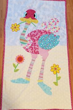 a quilted wall hanging with an ostrich on it's side and flowers in the background