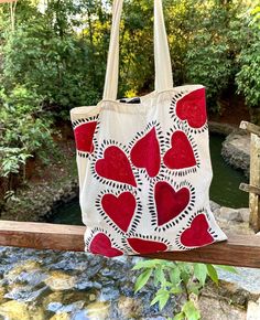 a white bag with red hearts on it hanging from a wooden rail next to a river