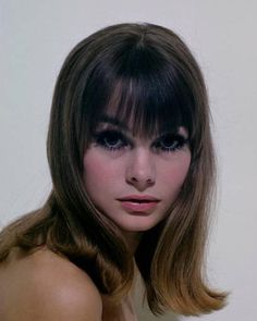 a woman with long hair and bangs is posing for the camera in front of a white wall