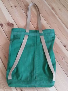 a green tote bag sitting on top of a wooden floor next to a pair of scissors