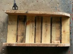 a wooden shelf with scissors hanging from it's sides on the wall next to a concrete floor