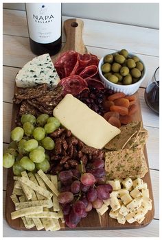 an assortment of cheeses, crackers and grapes on a wooden platter