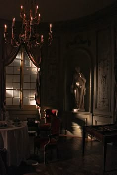 a dark room with a chandelier, table and chairs