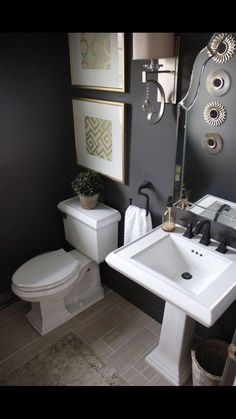 a white toilet sitting next to a sink in a bathroom under pictures on the wall