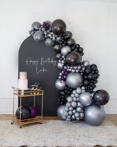 a black and silver balloon arch with happy birthday cake written on the wall next to it