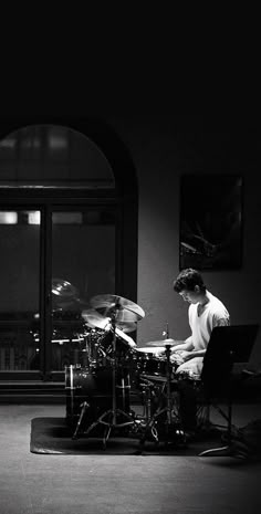 a man sitting at a table playing drums in front of a piano and another person standing behind him