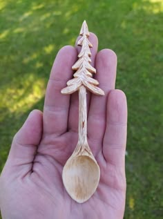 a hand holding a wooden spoon with a tree on it