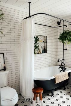 a bathroom with a black and white bathtub next to a toilet, shower curtain and stool