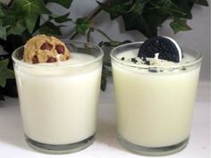 two glasses filled with milk and cookies on top of a white table next to green leaves