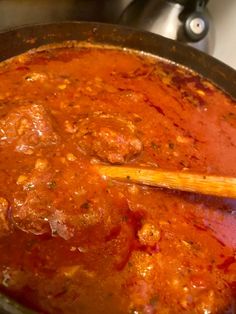 a pot filled with meat and sauce on top of a stove next to a wooden spoon