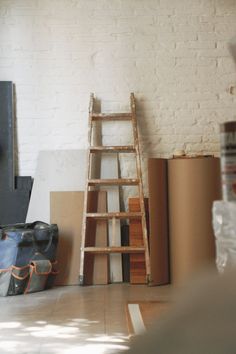 a ladder leaning against a white brick wall next to boxes and other items on the floor