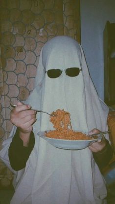 a person in a ghost costume is eating spaghetti from a plate with sunglasses on their head