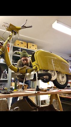 a man working on a yellow motorcycle in a garage with shelves and boxes behind him