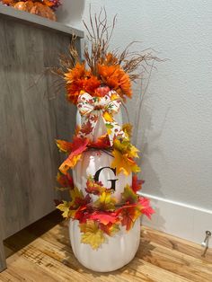 a white pumpkin decorated with fall leaves and a monogrammed g on the front