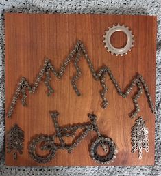 a wooden plaque with metal chains and bicycle parts attached to the front of it on a carpeted surface