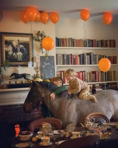 two children are sitting on top of a fake horse in the middle of a room with bookshelves and balloons