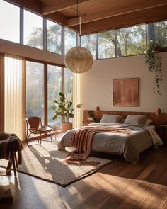 a bedroom with wooden floors and large windows overlooking the trees in the distance is shown