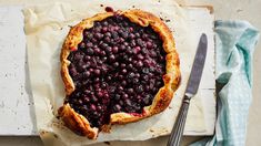 a pie with blueberries on it sitting on top of a table next to a knife and fork