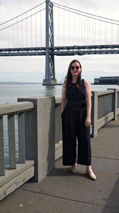 a woman standing on the side of a bridge next to water and a bridge in the background