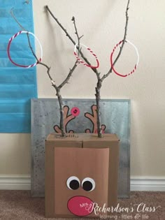 a cardboard box with branches in it and a reindeer face on the front, sitting next to a window