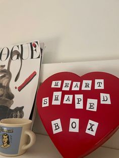 a red heart shaped box next to a coffee cup and magazine on a white shelf