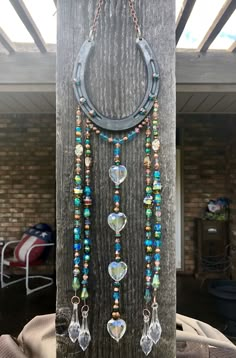 a piece of jewelry is hanging on a wooden post with beads and chains attached to it