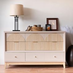 a white dresser sitting on top of a wooden floor next to a lamp and framed pictures