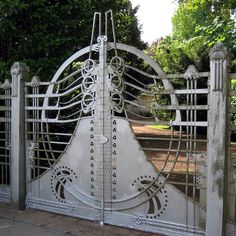 an iron gate with intricate designs on the top and bottom, surrounded by greenery