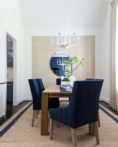 a dining room table with blue chairs and a round mirror on the wall above it