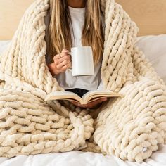 a woman is sitting in bed wrapped up with a blanket and holding a coffee mug