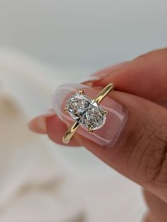 a woman's hand holding an engagement ring with two diamonds on it and the middle one in yellow gold